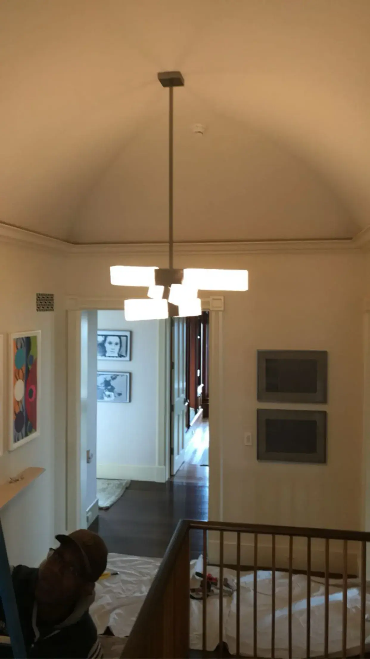 Electrician installing a modern chandelier in a finished stair hall
